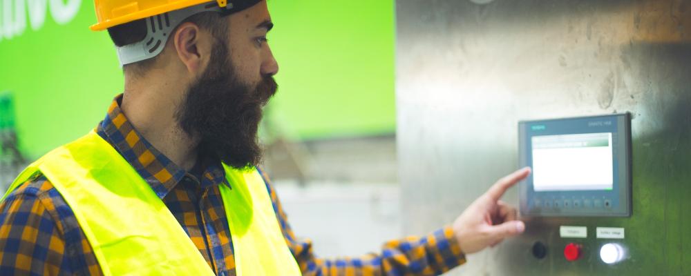 Man wearing hardhat touching equipment control screen 